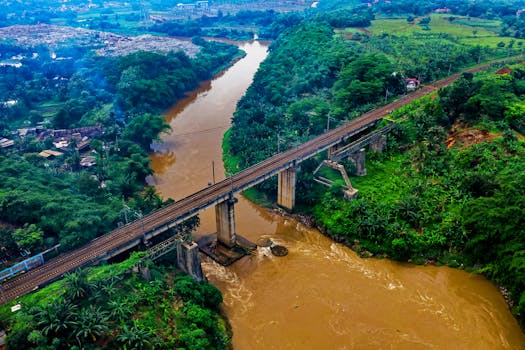 Scenic aerial view of a railway bridge crossing over a lush green river landscape in Sindang Jaya, Indonesia.