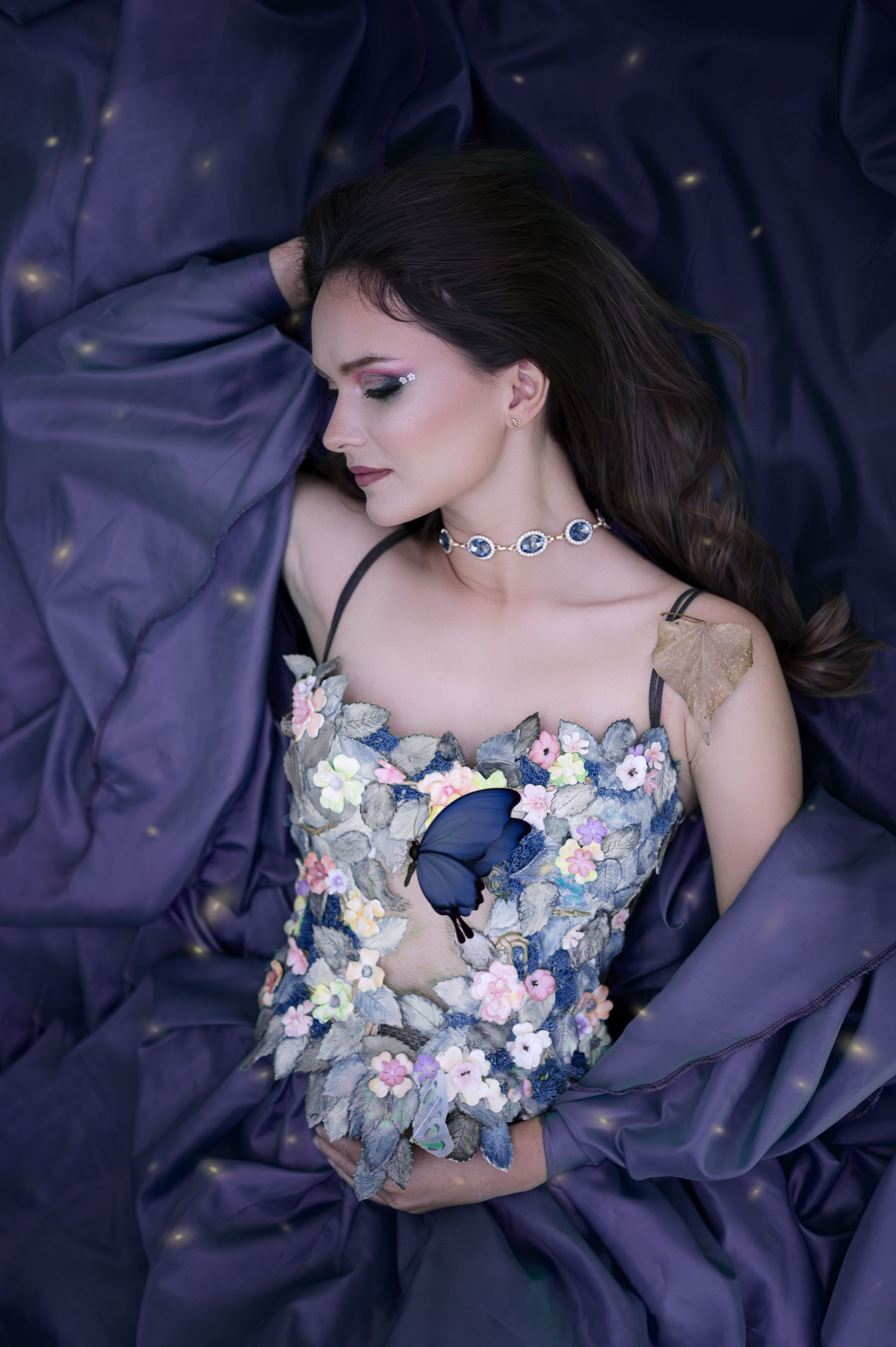 Elegant woman in a floral corset with a butterfly, lying amidst draped fabric.