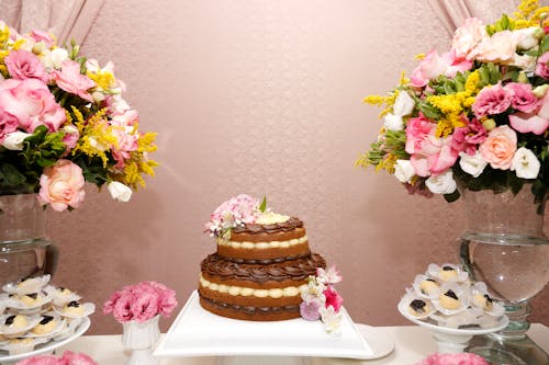 2つの盛り合わせフラワーブーケの横にある丸い2層チョコレートケーキ