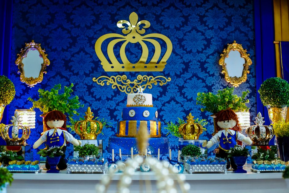 Royal themed dessert table with cake decorations, crowns, and plush dolls.