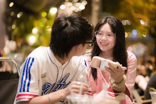 Young couple smiling and talking with cellphone in a vibrant outdoor setting at night.
