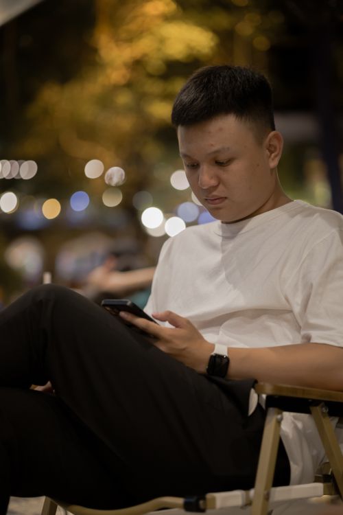 Free Young man in white t-shirt using smartphone outdoors at night. Stock Photo