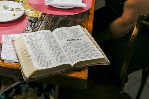 Фотография открытой книги Библии на коричневом столе