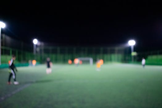 Blurred image of a nighttime football match under bright stadium lights with players on the field.