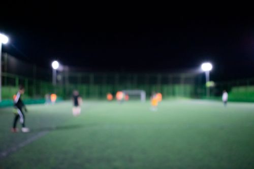 Free Blurred image of a nighttime football match under bright stadium lights with players on the field. Stock Photo