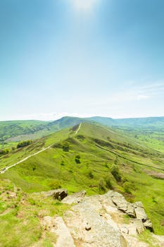 Scenic aerial view of green hills and valleys in Hope Valley, England under a clear blue sky.