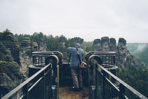 Free A lone photographer taking pictures of a breathtaking cliffside view amidst a misty forest landscape. Stock Photo