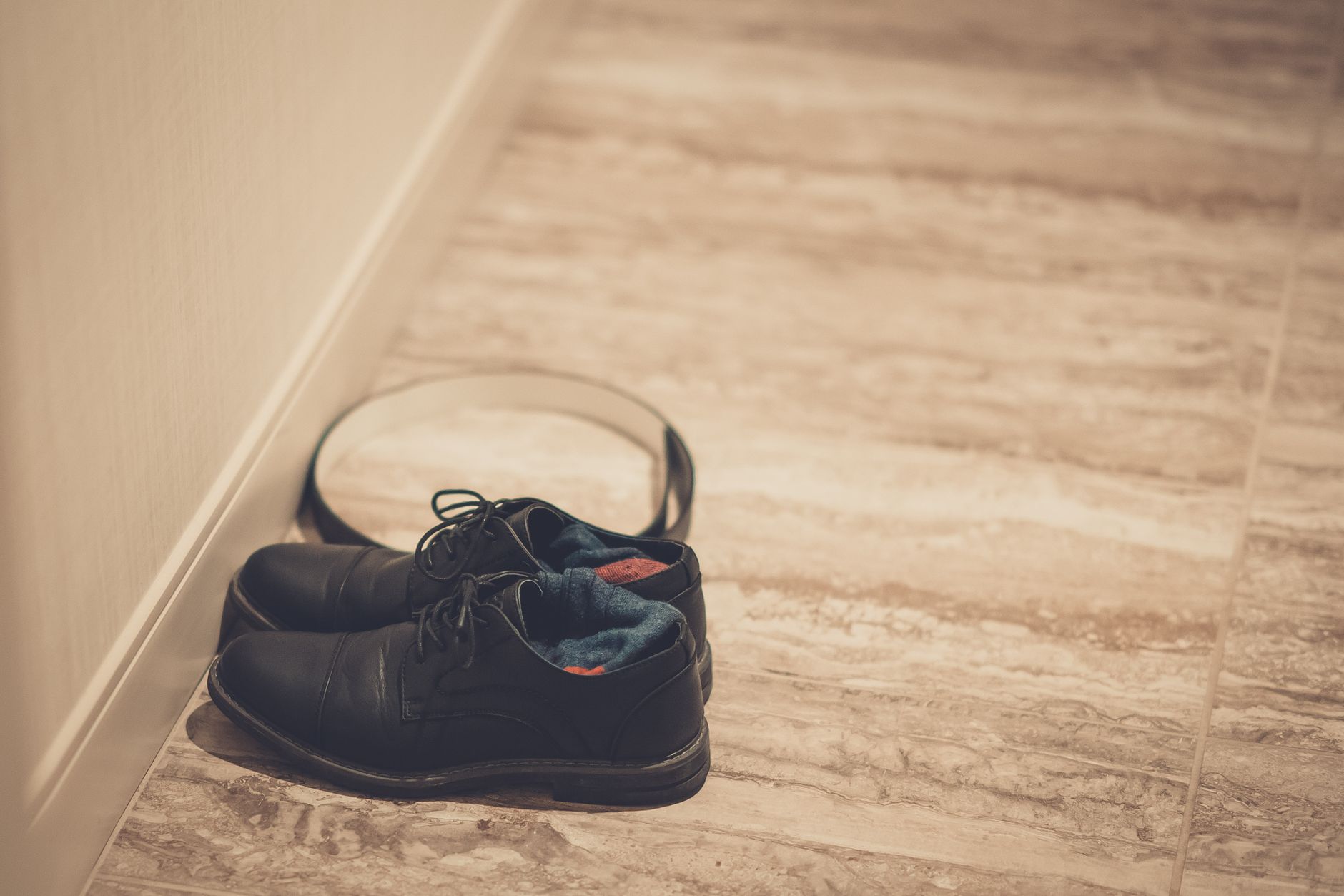 Elegantly arranged black leather shoes with blue socks on a wooden floor, featuring a stylish belt.