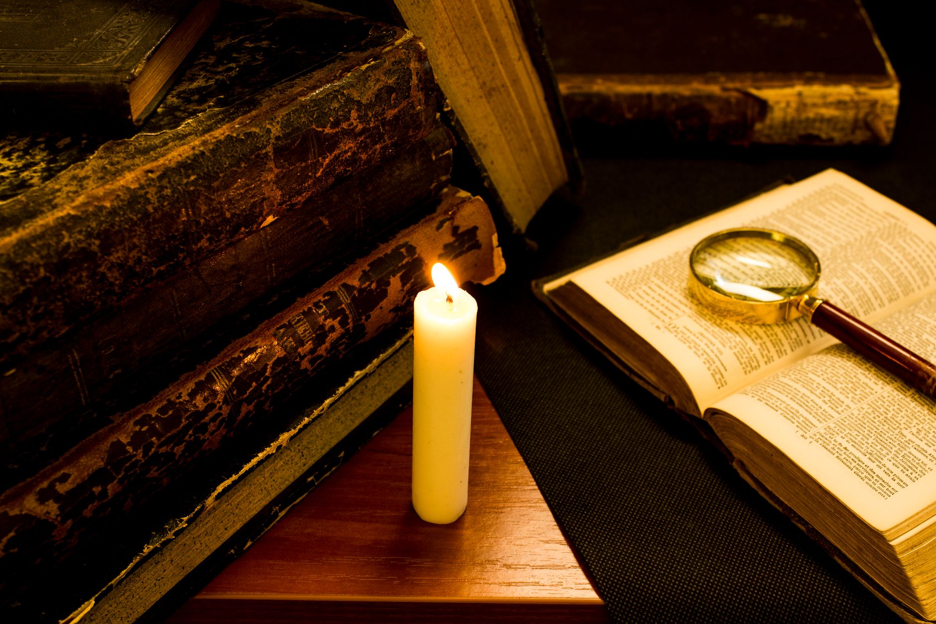 Cozy candlelit vignette with vintage books and magnifying glass, evoking a sense of history and mystery.