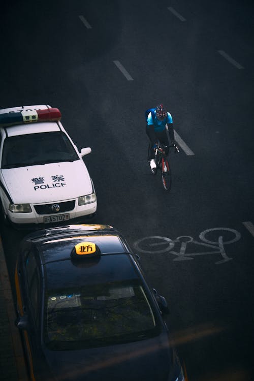 Man on Road Bike Cycling near Parked Taxi and Police Cars