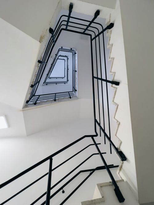 Free A unique perspective of a modern staircase design with black handrails, emphasizing architectural lines. Stock Photo