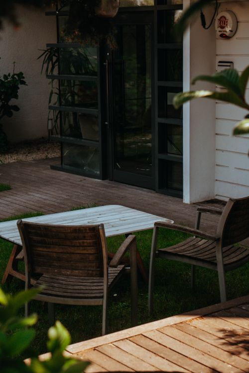 Free A tranquil outdoor patio featuring wooden chairs and table with greenery surrounding. Stock Photo