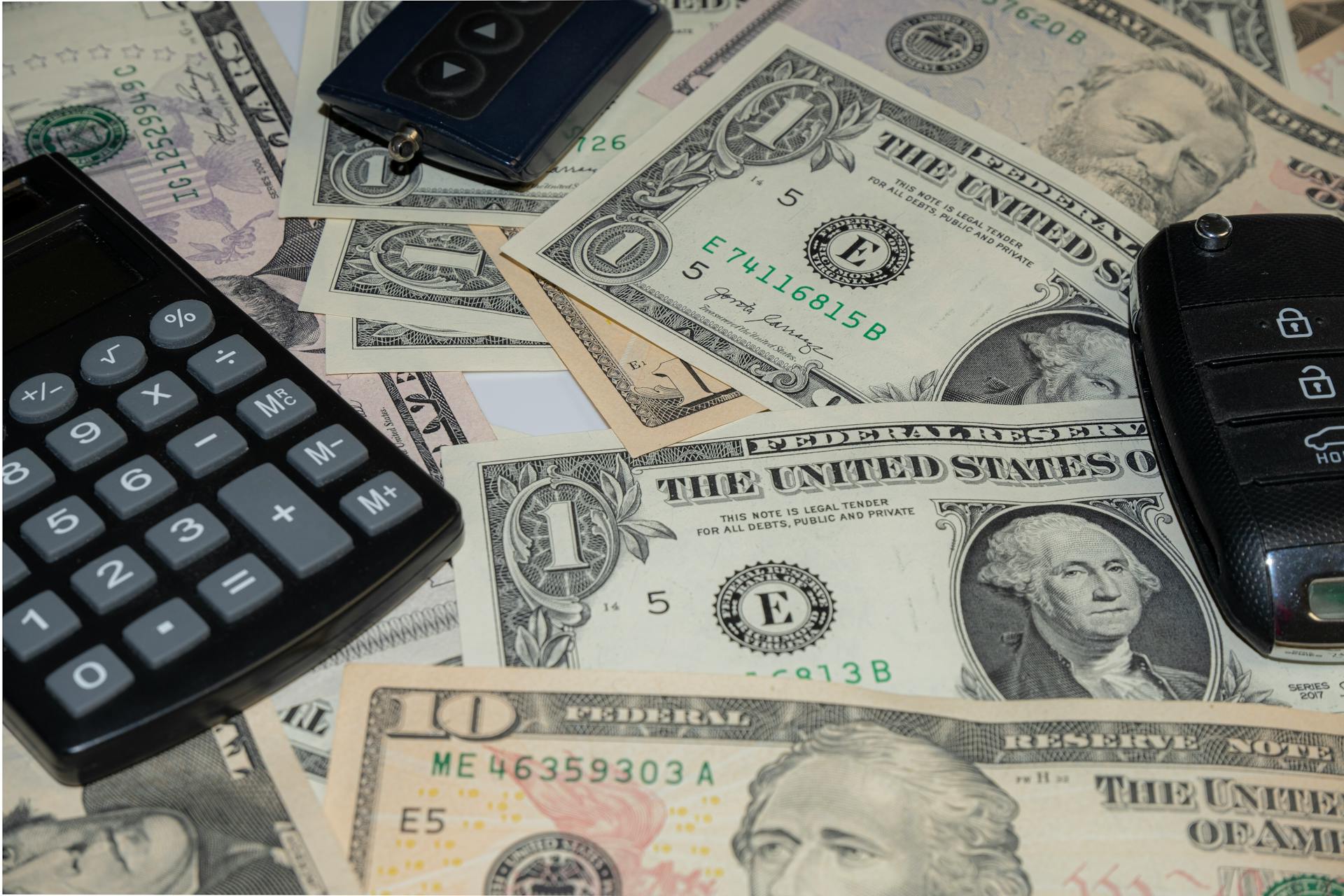 Close-up of various US banknotes, calculator, and car key illustrating finance concept.