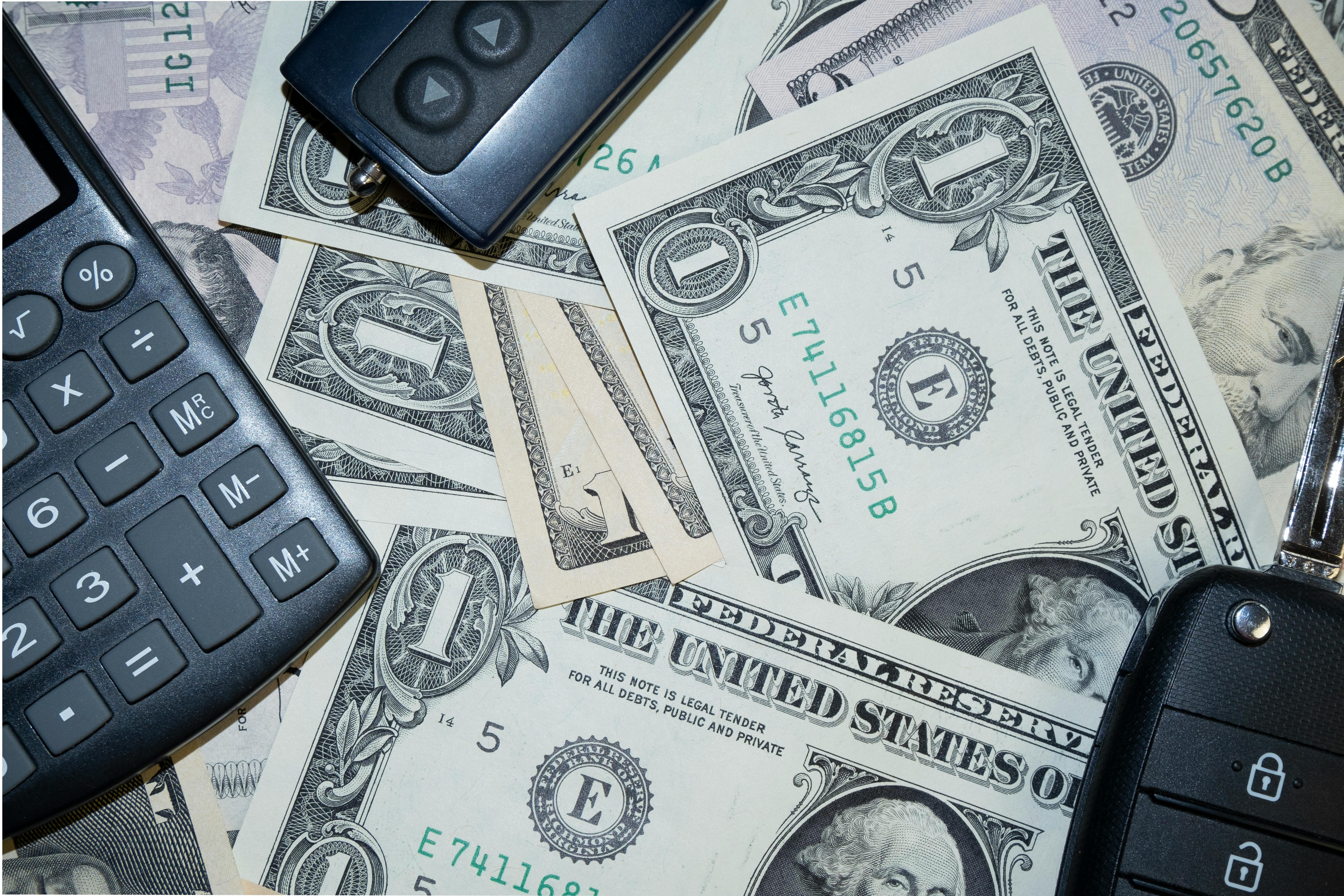 An arrangement of US dollar bills, car keys, and a calculator representing finance and investment concepts.