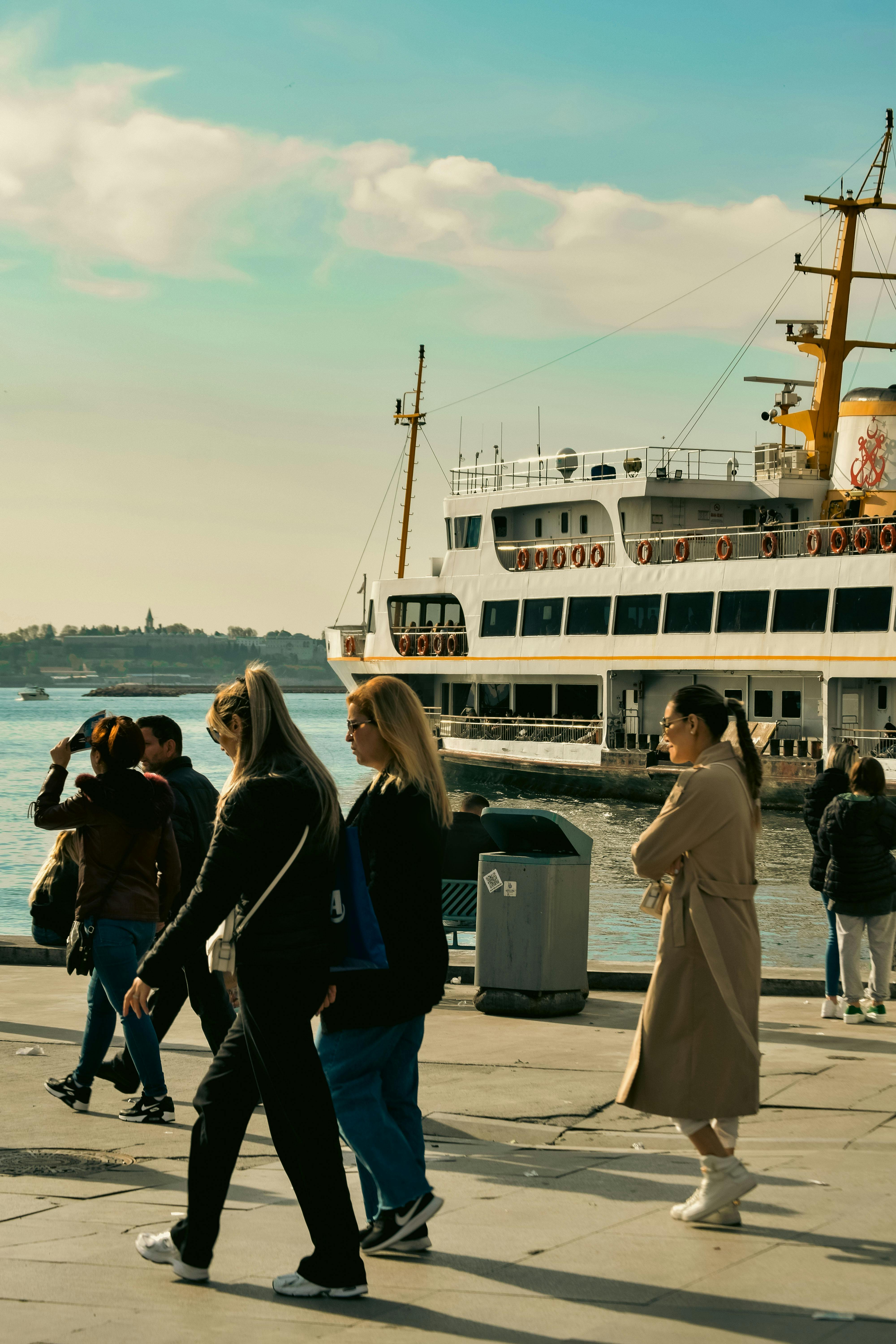 Free A bustling pier scene with people walking by a ferry on a sunlit day, capturing urban life. Stock Photo