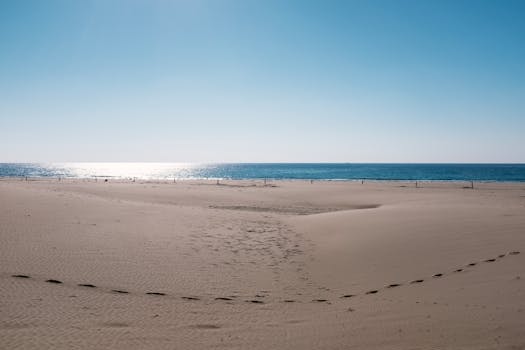 Serene beach view at Kaş, Antalya with calm waves and footsteps in the sand under a clear sky.