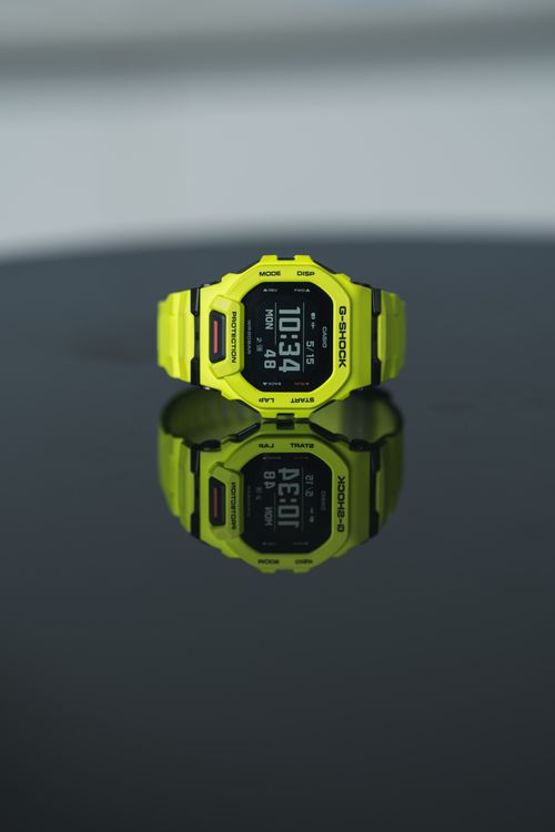Free A vibrant yellow digital watch displayed on a glossy black surface, showing time clearly. Stock Photo