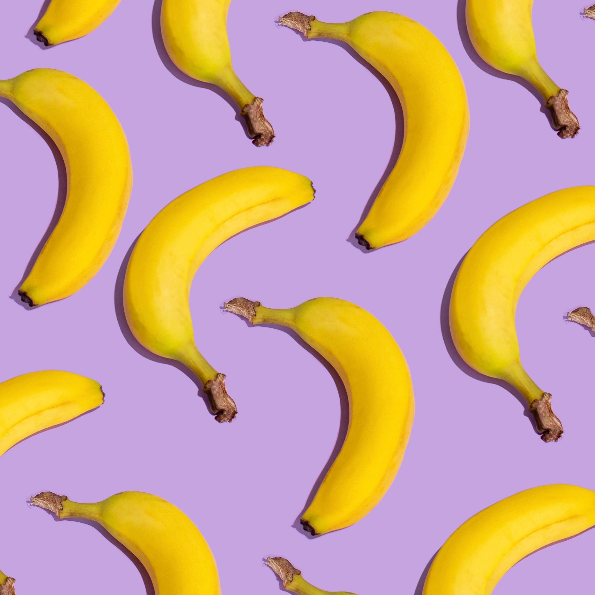 Bright yellow bananas arranged on a purple surface in a playful flat lay pattern.