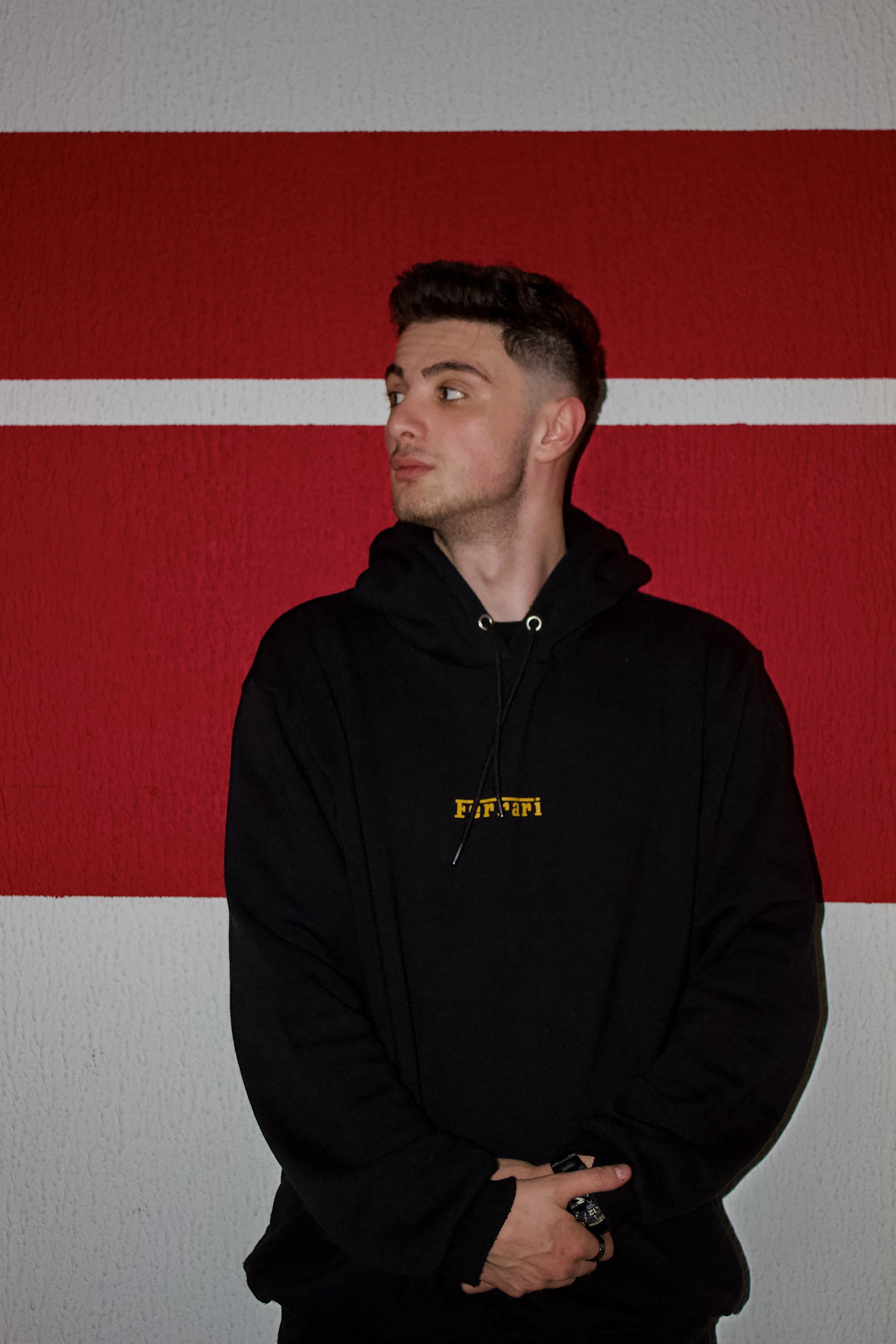 Portrait of a fashionable man in a black hoodie against a vibrant red backdrop.