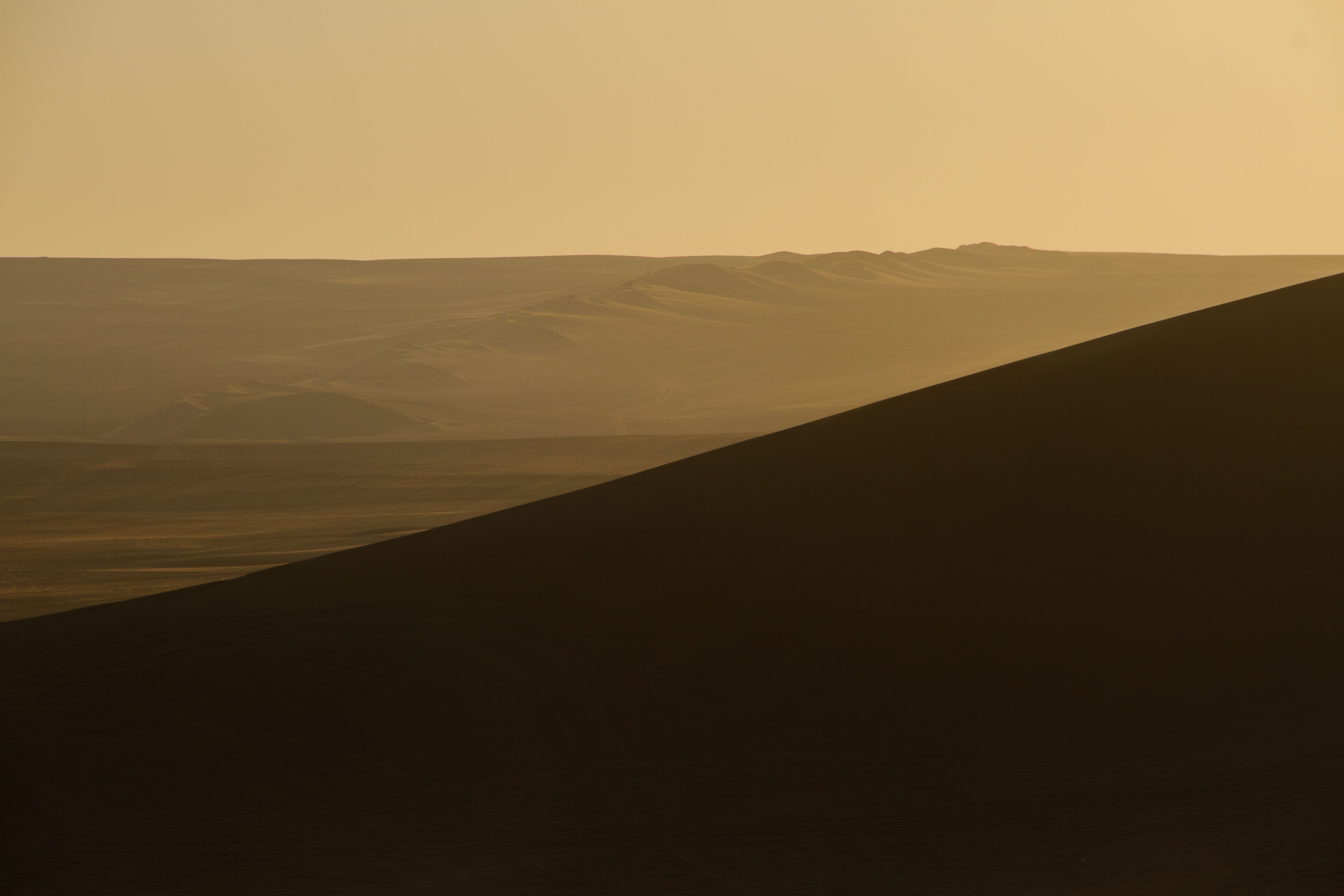 Capture the tranquility of a barren desert landscape with rolling hills at sunset.