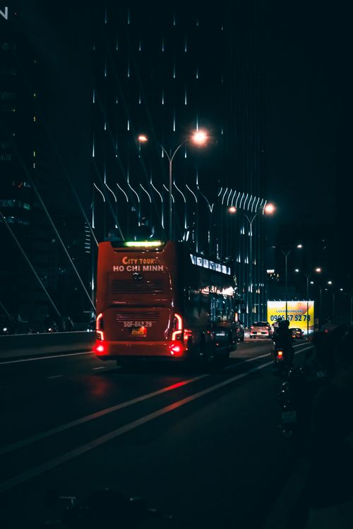 Free City tour bus on vibrant Ho Chi Minh street, illuminated by skyscrapers at night. Stock Photo