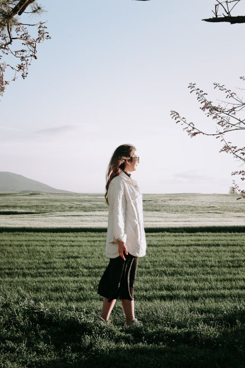Free A woman stands contemplatively in a green field during spring, wearing a white jacket. Stock Photo