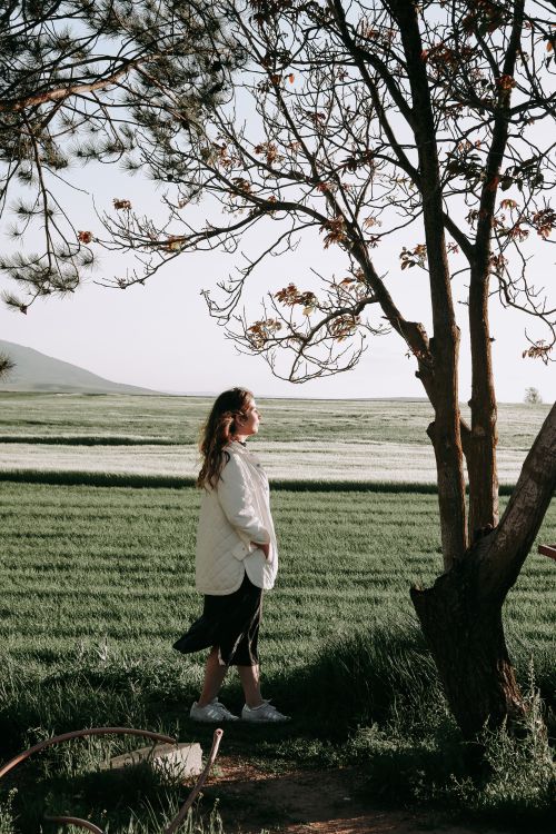 Free A woman stands peacefully in a grassy field, embracing the calm ambiance of nature during spring. Stock Photo