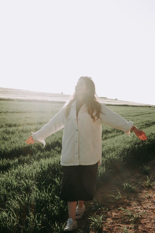 Free A woman enjoying the sunlight with open arms in a vast green field, embracing nature. Stock Photo