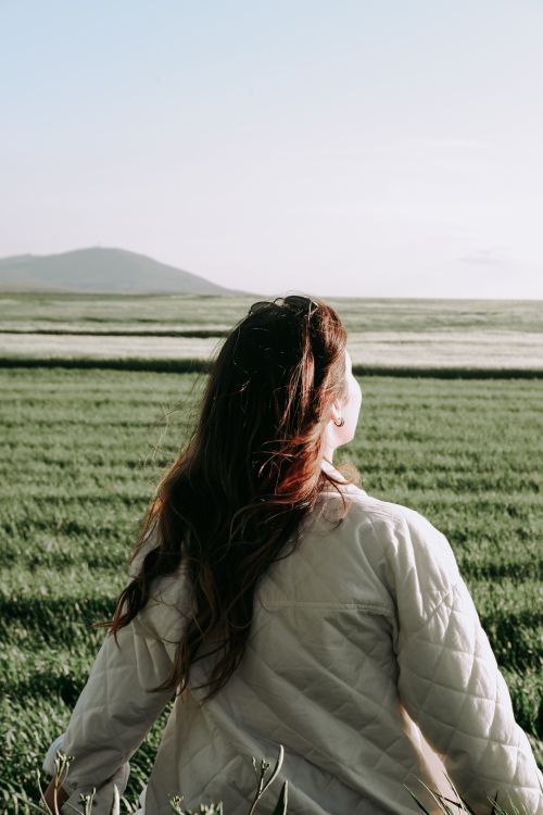 Free Back view of a young woman enjoying the serenity of a rural field during summer. Stock Photo