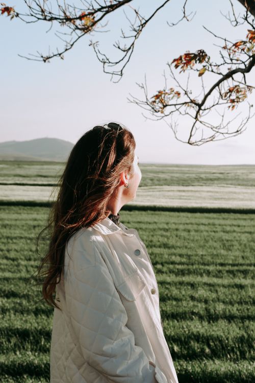 Free A woman in a white jacket admires the tranquil autumn rural scene. Stock Photo
