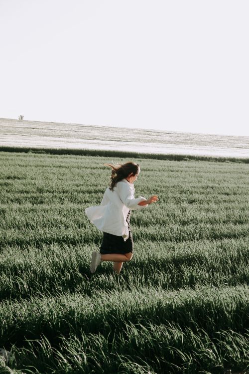 Free A woman in a white shirt running freely through a lush green field with a clear horizon. Stock Photo