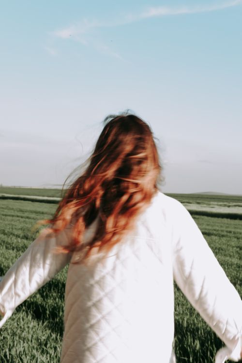 Free Back view of a woman with long hair enjoying a breezy day in a green field. Stock Photo