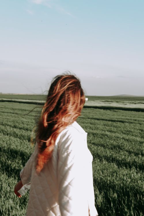 Free A woman with flowing hair stands in a lush green meadow under a clear sky. Stock Photo