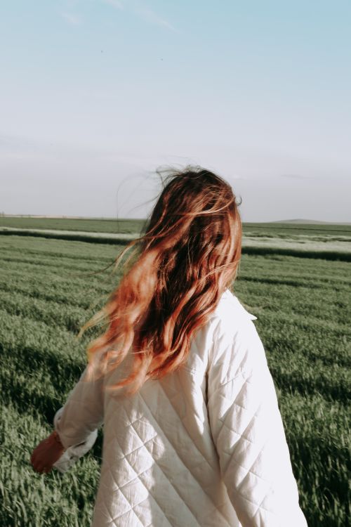 Free Woman with flowing hair enjoying a walk through a lush green field on a sunny day. Stock Photo