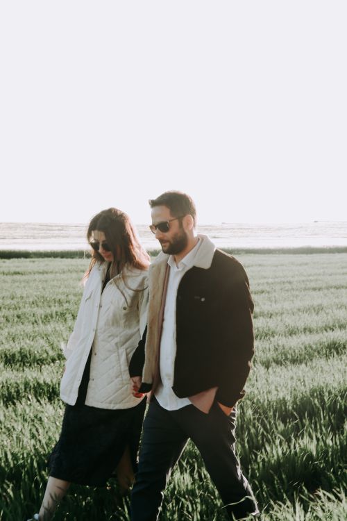 Free Couple walking hand-in-hand in a rural field, showcasing fashion style and sunlight. Stock Photo