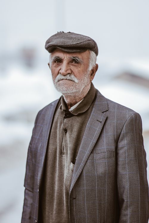 Free Portrait of an elderly man standing outdoors wearing a suit and flat cap. Stock Photo