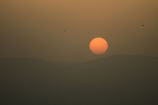 A tranquil sunset scene with birds flying over misty hills, casting a warm glow.