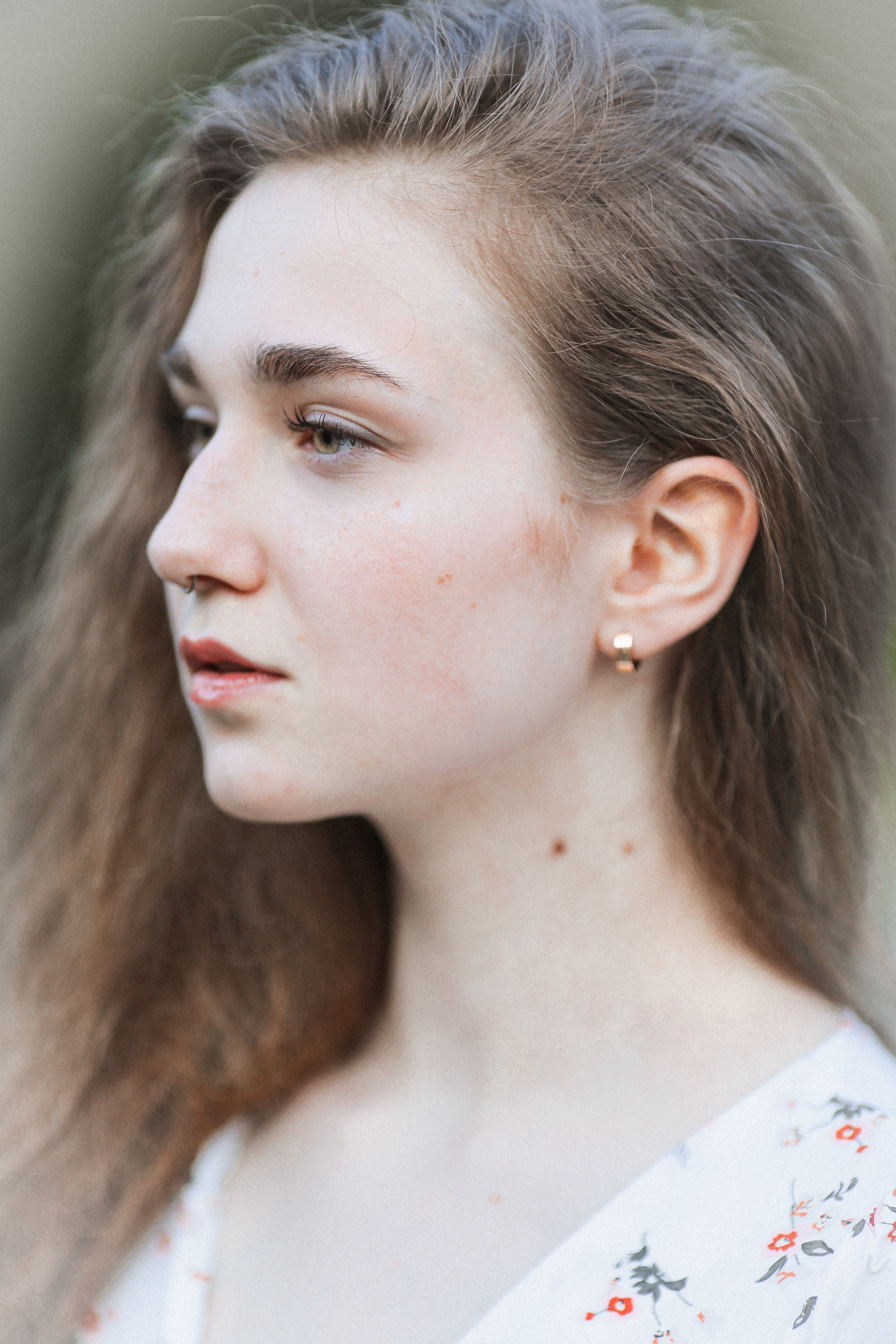 Side profile of a young woman with long hair and earrings, captured in natural light.