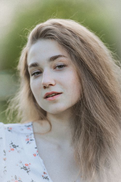 Free A serene outdoor portrait of a young woman with long hair, wearing a floral dress. Stock Photo