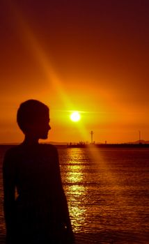 Stunning silhouette of a person against a vibrant orange sunset over the ocean, creating an idyllic and scenic view.