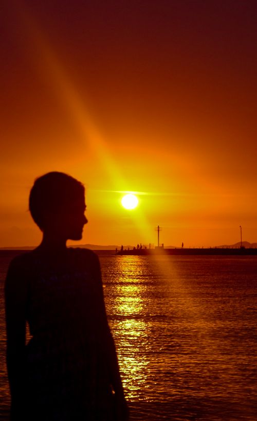 Free Stunning silhouette of a person against a vibrant orange sunset over the ocean, creating an idyllic and scenic view. Stock Photo