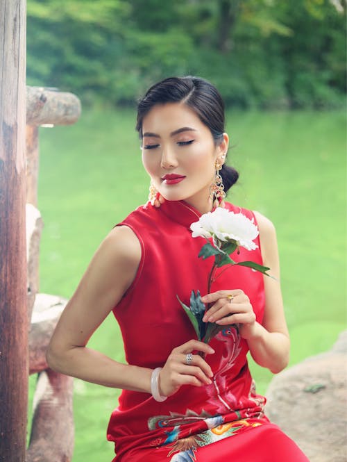Portrait of a Female Model Wearing a Red Dress Sitting Outdoors with a White Flower in Hands