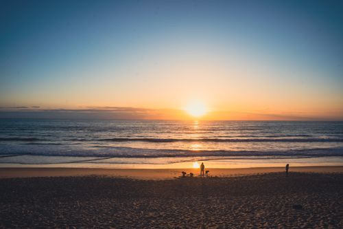 Free A peaceful beach scene at sunset with the sun dipping below the horizon. Stock Photo