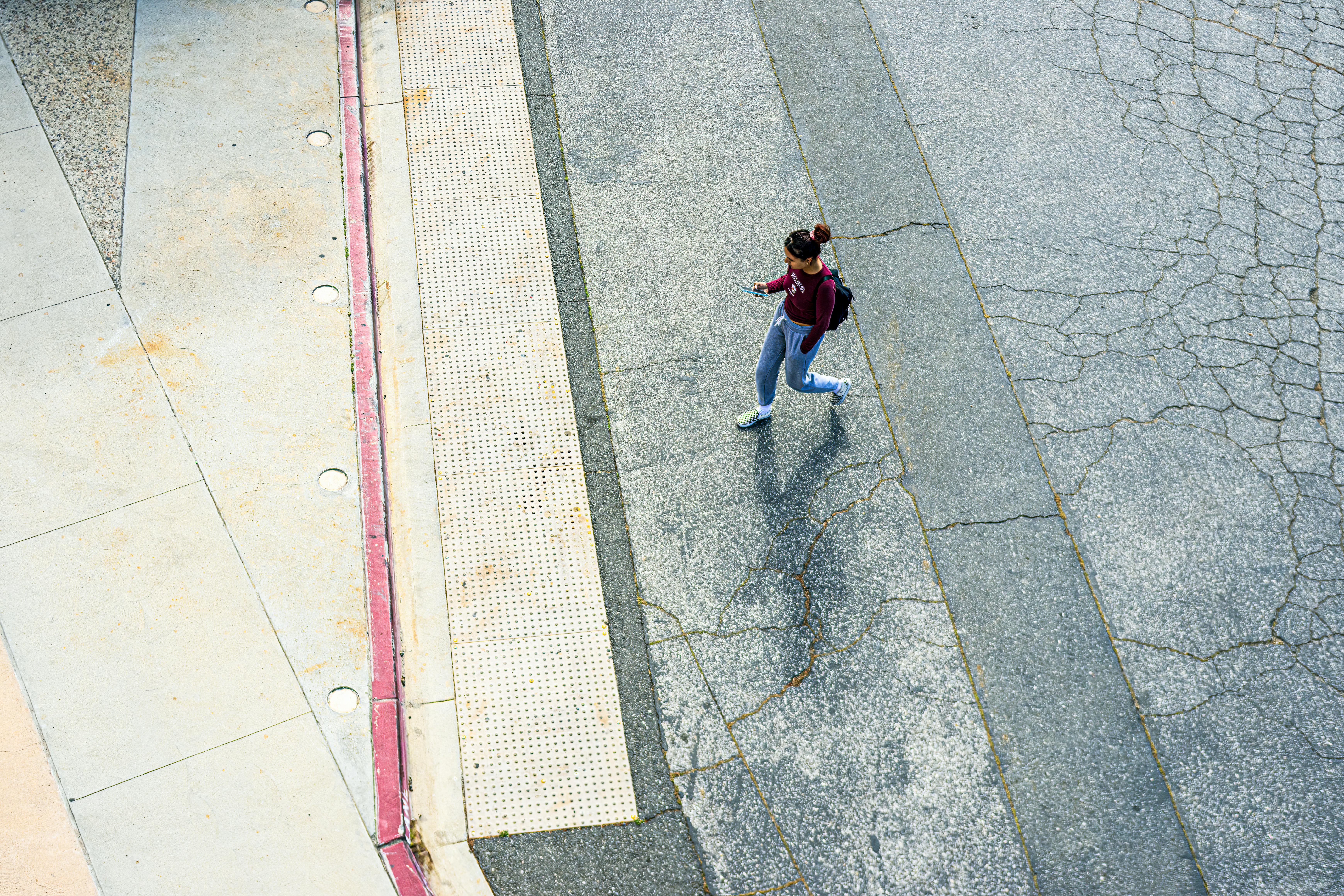 Aerial view of a woman walking on city pavement, captured from above.