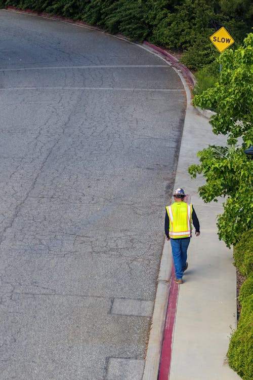 High Angle Shot of a Construction Worker in a Reflective Vest and Helmet Walking on the Sidewalk 