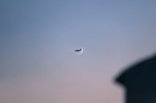 Airplane Flying over Crescent on Clear Sky