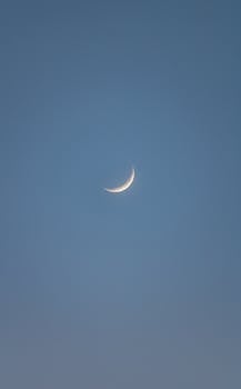 A serene crescent moon against a clear blue sky during evening twilight.