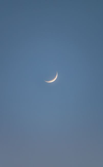 A serene crescent moon against a clear blue sky during evening twilight.