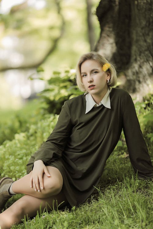Young Blonde Woman in Dress with White Collar Sitting by Tree