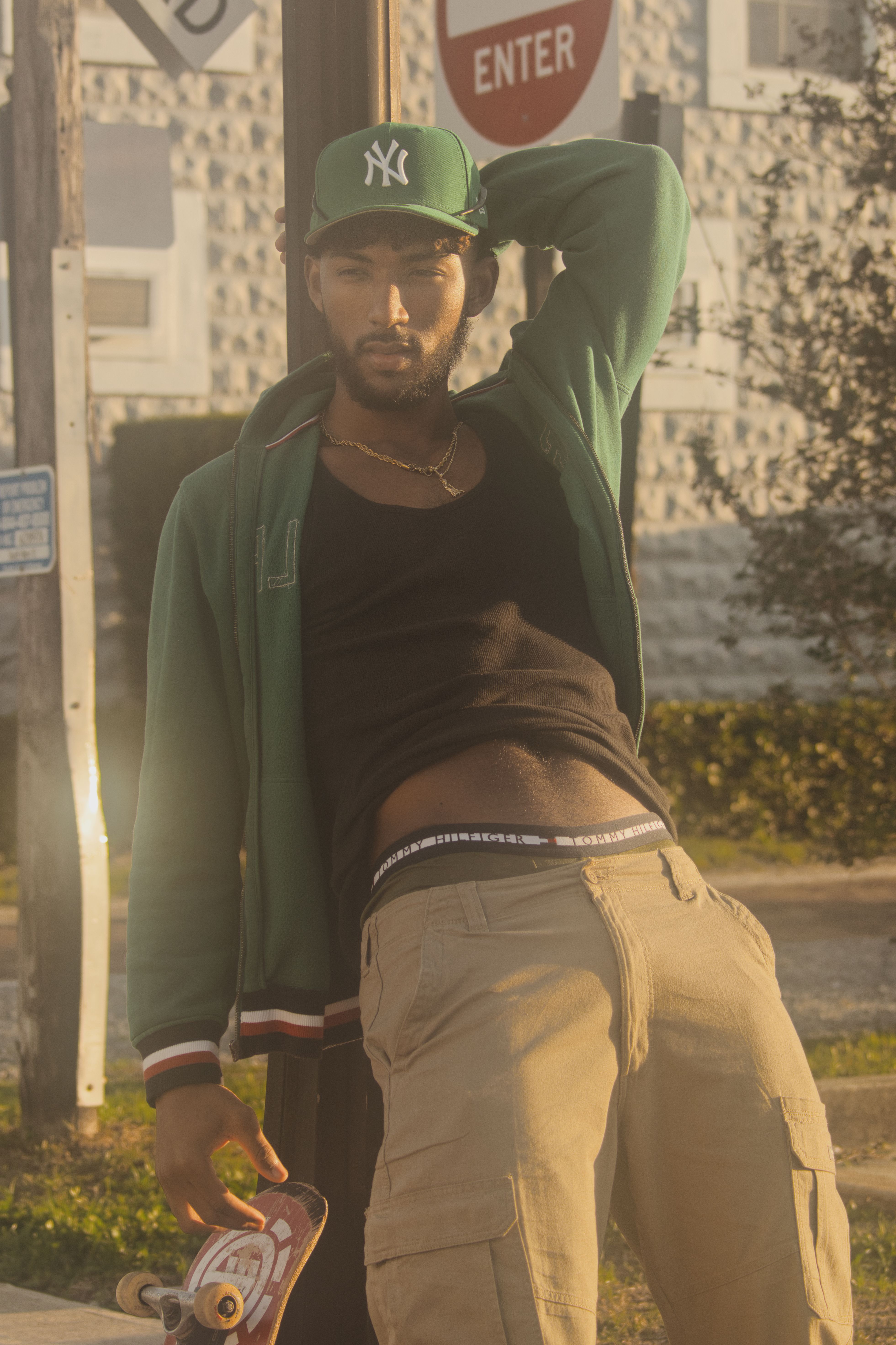 Stylish man in streetwear poses confidently holding a skateboard in an urban setting.